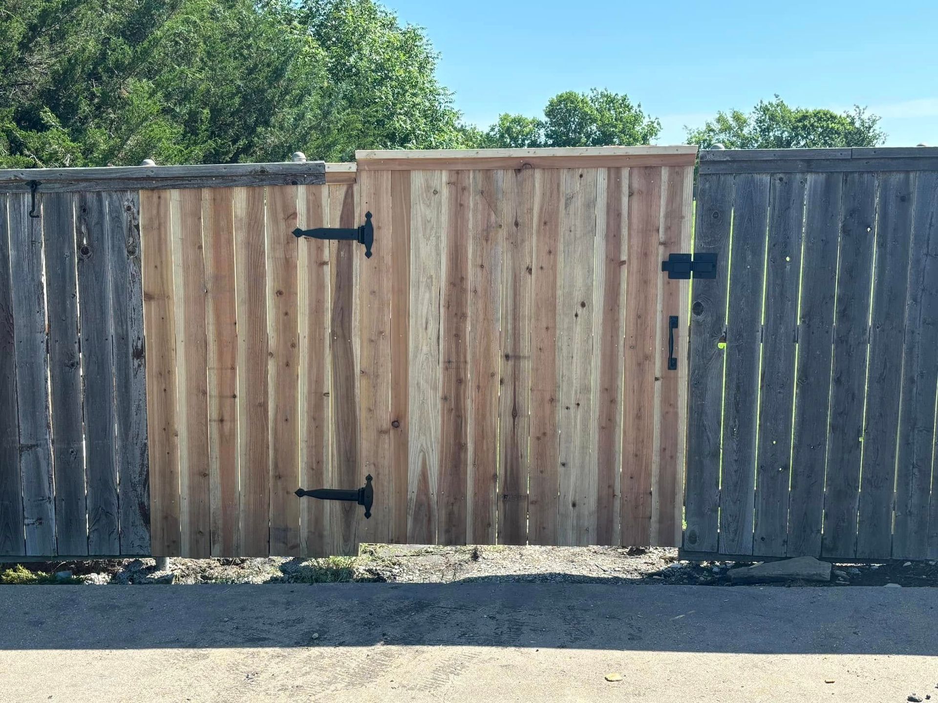 A wooden gate, newer and lighter in color, sits between two weathered gray fences.