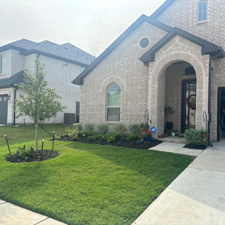 A well-manicured suburban home with light brick, arched entry, and a vibrant green lawn on a cloudy day.