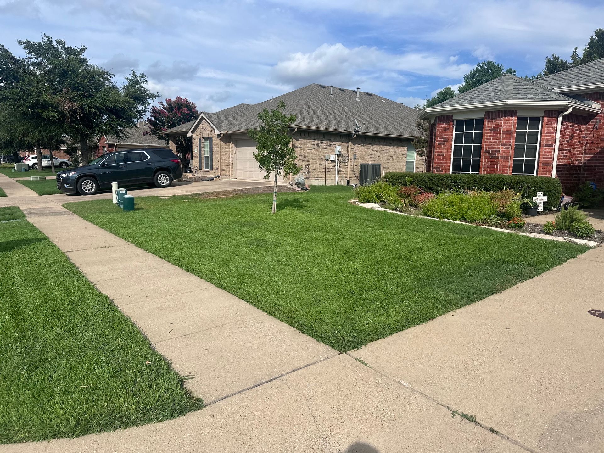 Suburban street with well-manicured lawns and houses. A car is parked on the left. Sunny day.
