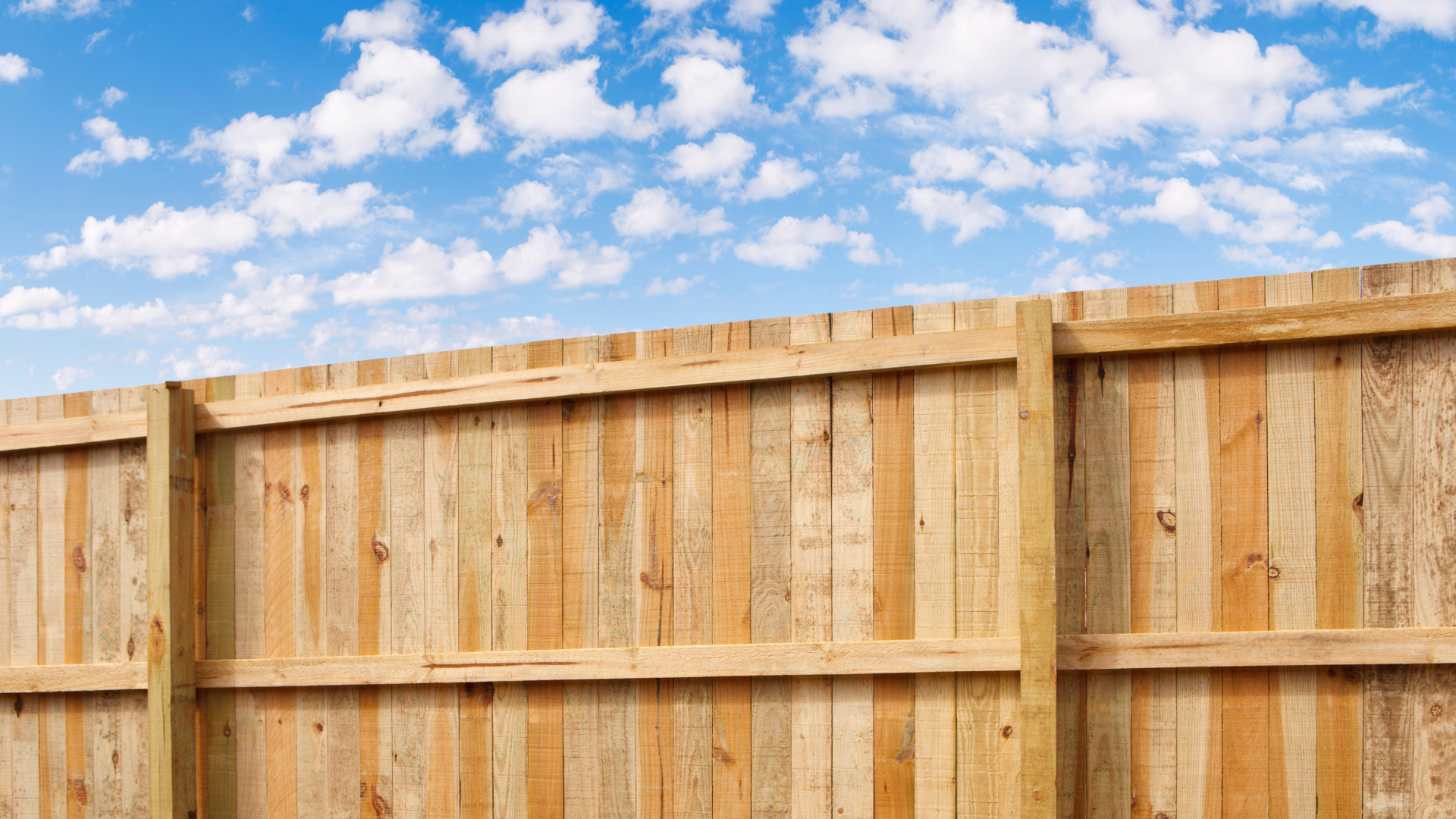 Wooden fence against a blue sky with fluffy white clouds.