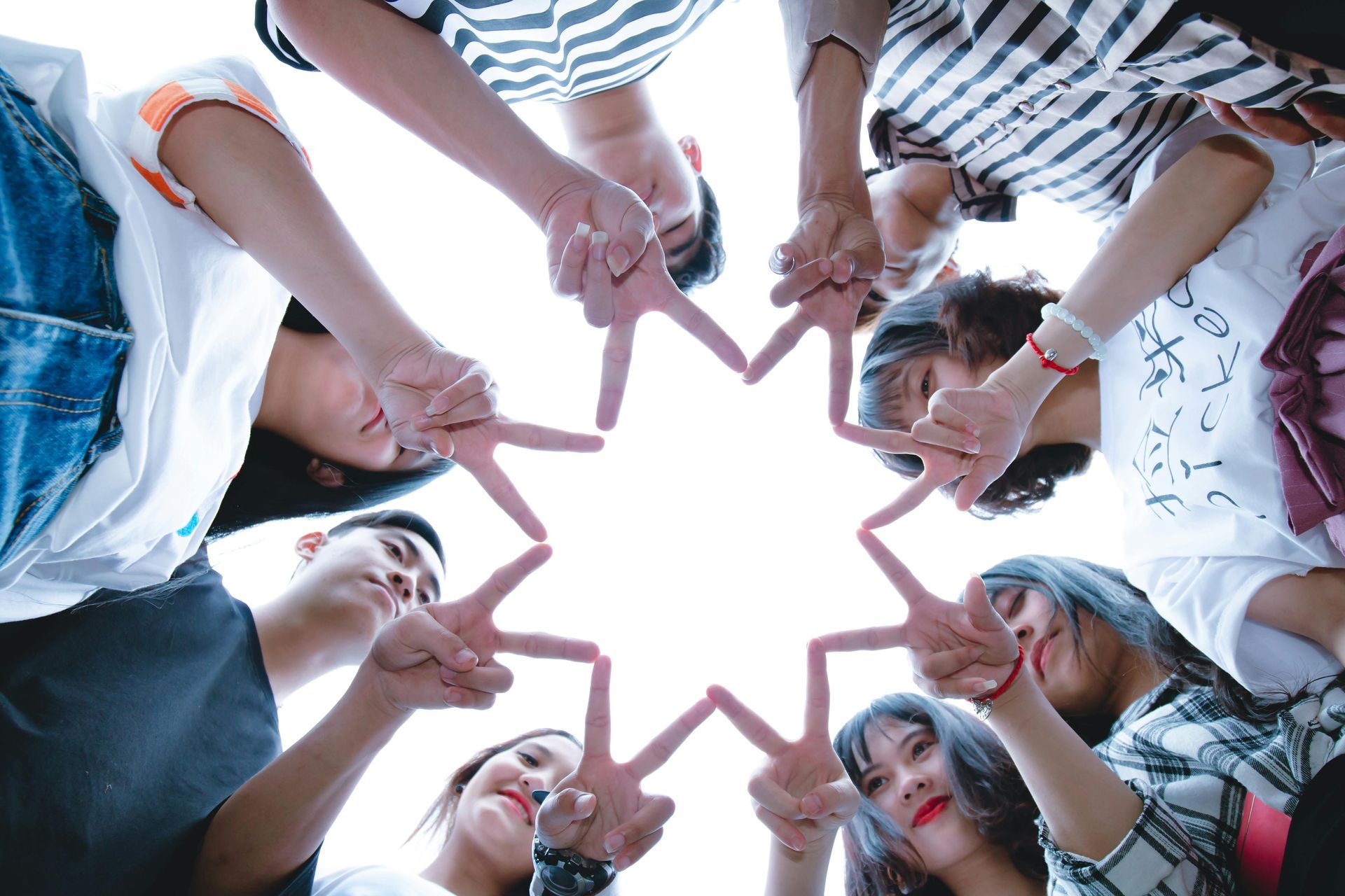 a group of youth making a star shape with their fingers, the camera looking up at them from the ground