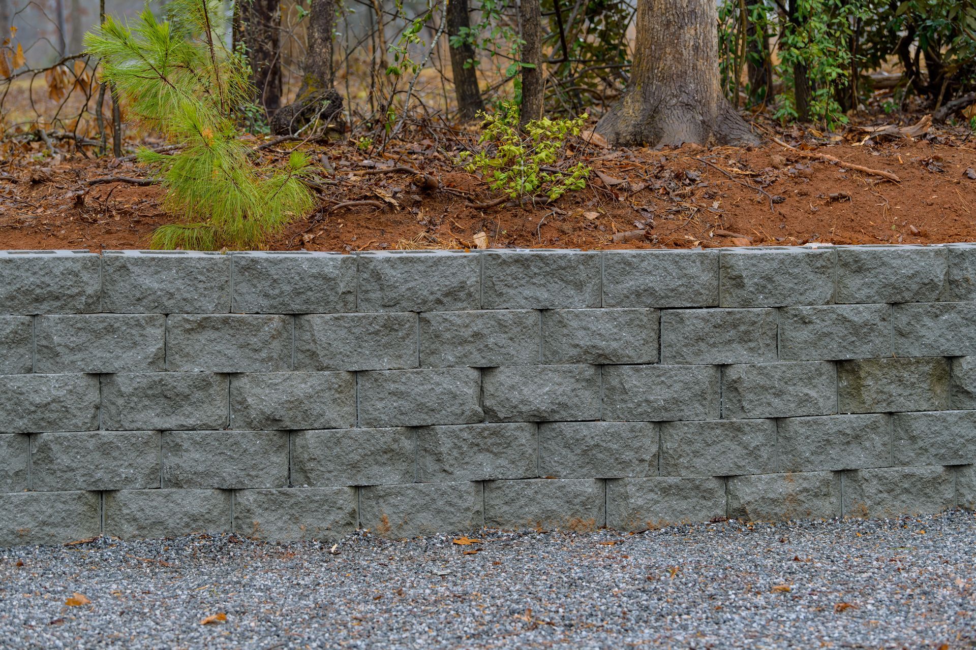 A brick wall is surrounded by gravel and trees.