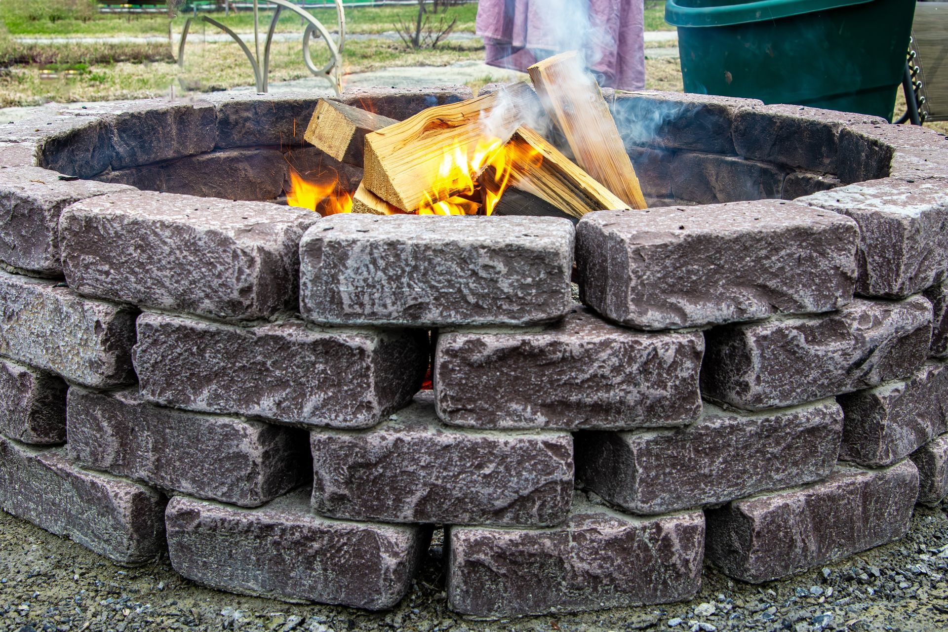 Fire pit made of dark gray bricks with a fire burning inside, outdoor setting.