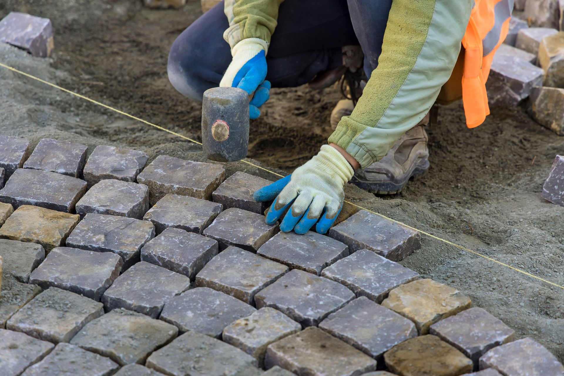 A man is laying bricks on a sidewalk with a hammer.