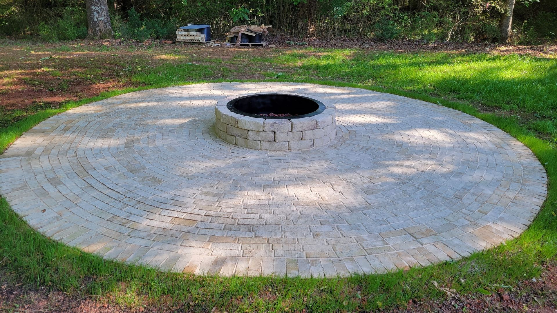 Large circular stone fire pit or memorial ring in a grassy park with a dark center opening