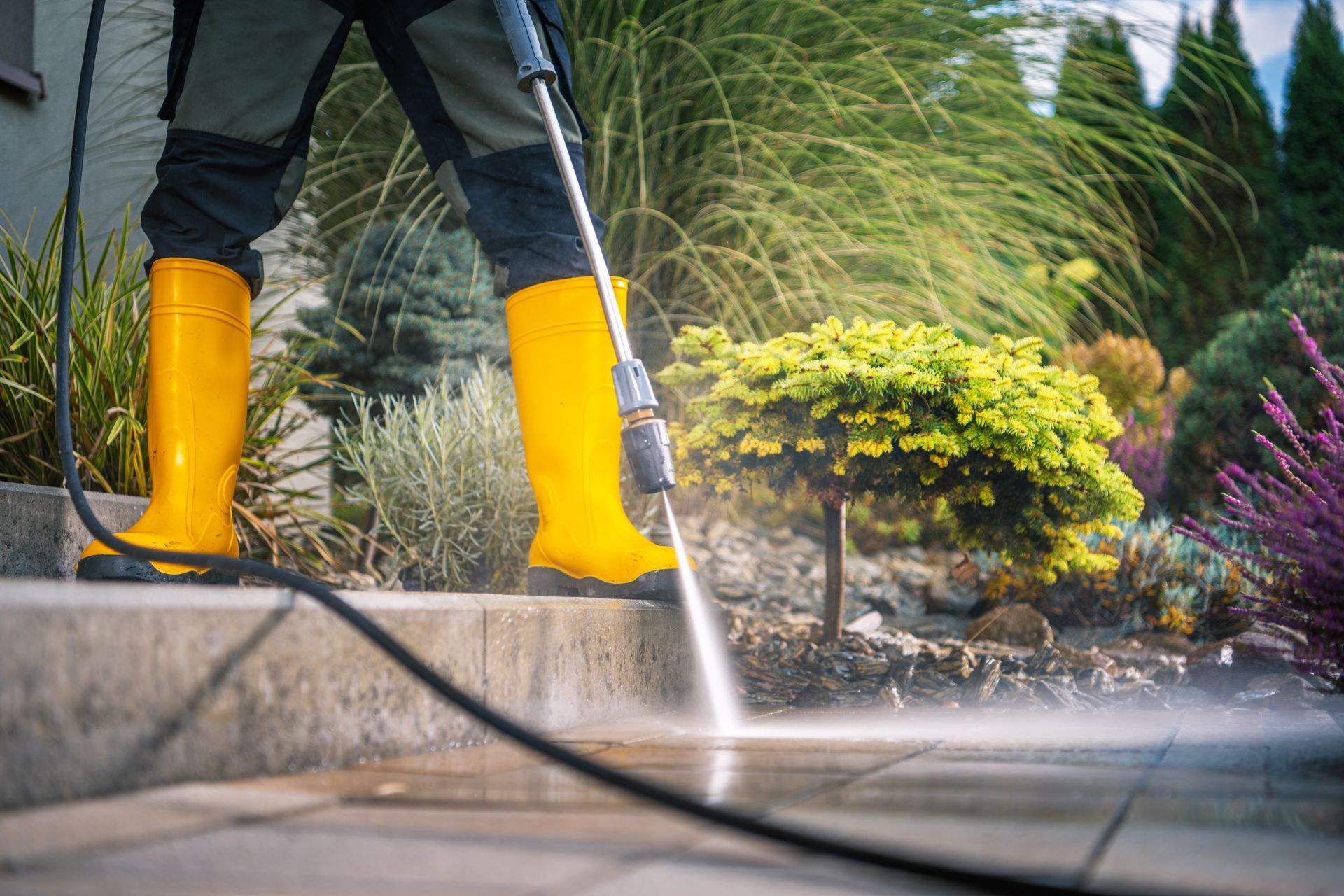 Person in yellow boots power washing a concrete patio outdoors.