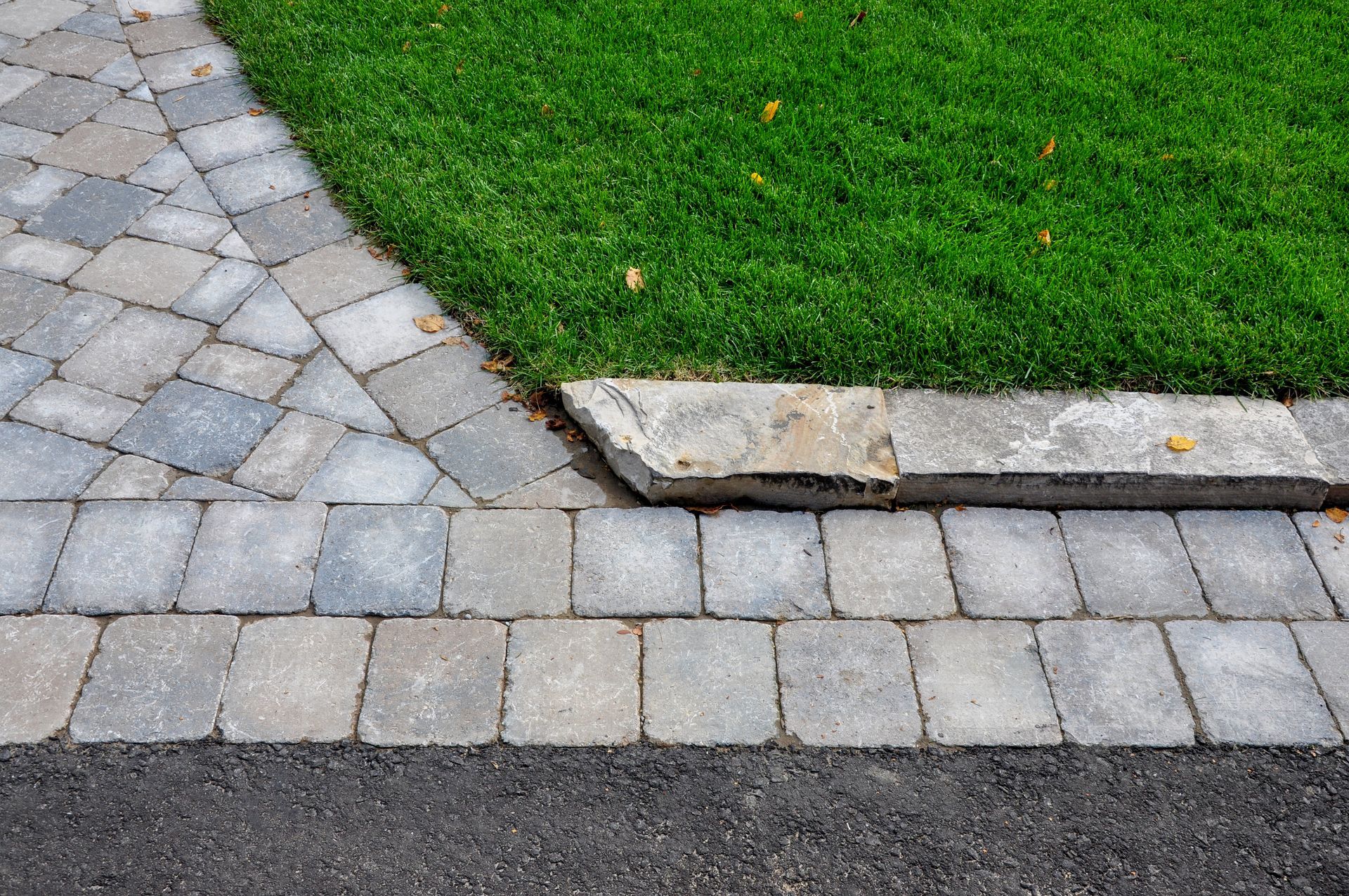 Curved stone walkway beside green grass and a broken curb edge