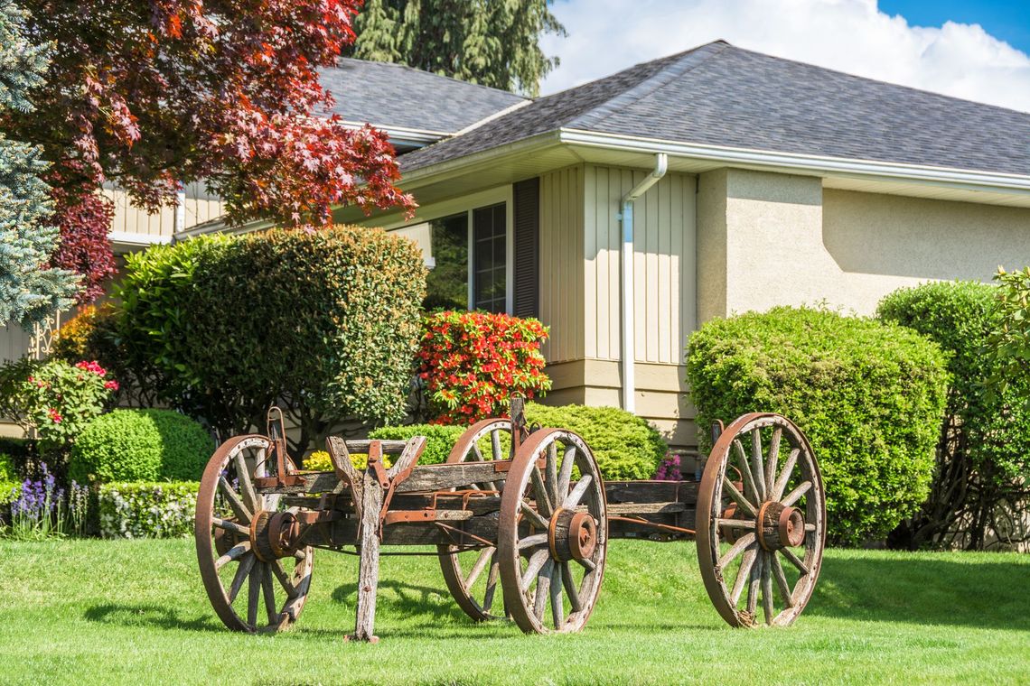 Two wooden wagon wheels are sitting in the grass in front of a house.