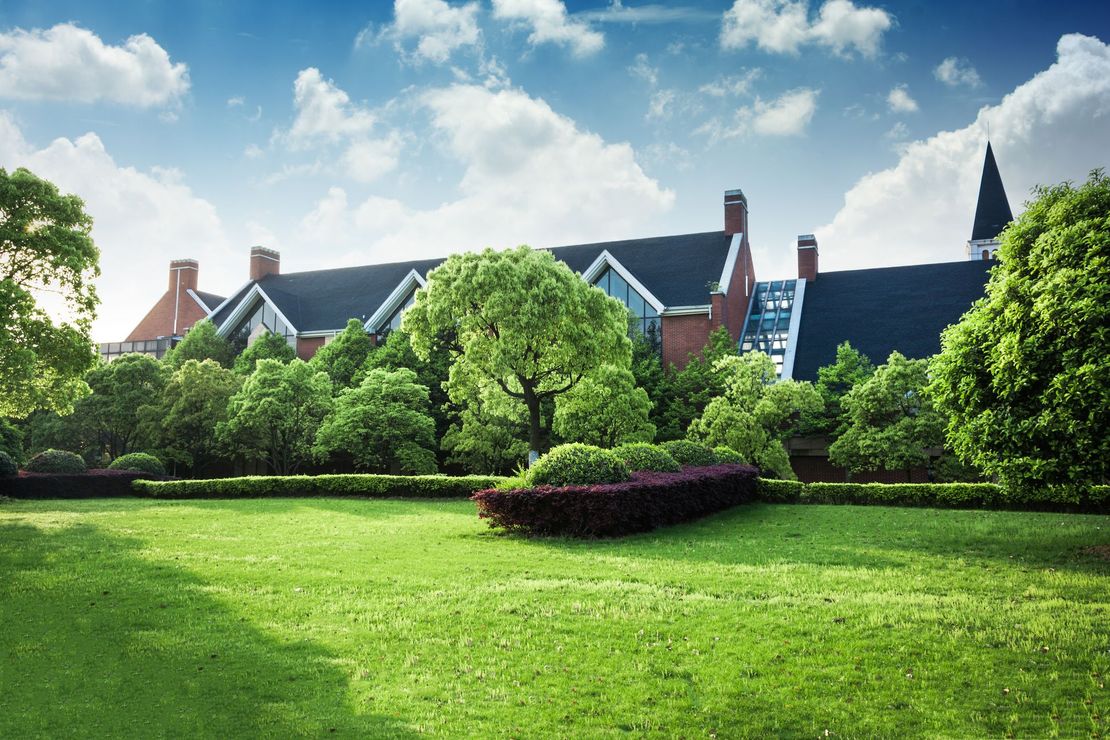 A large house is surrounded by trees and a lush green field.