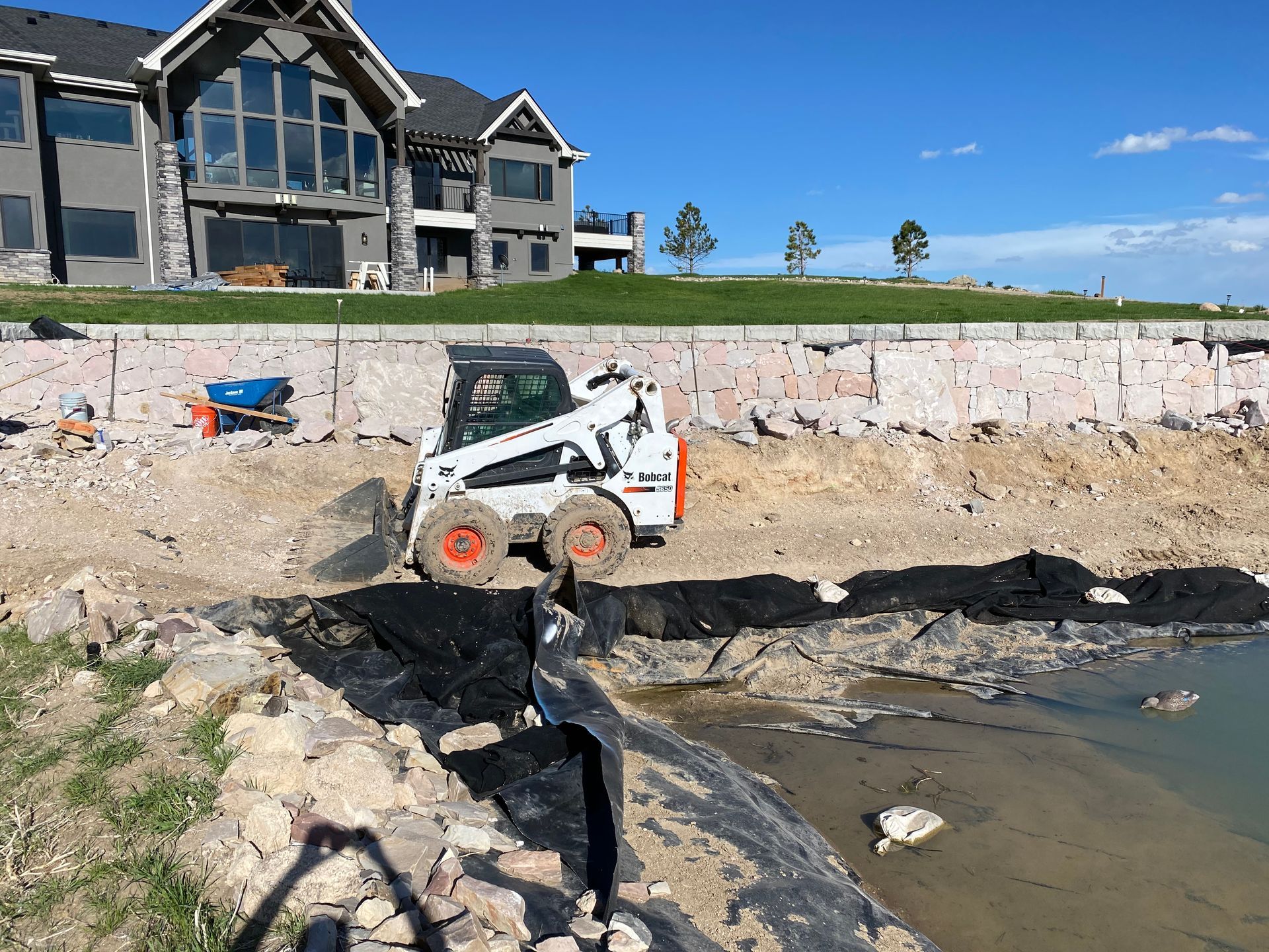 A bobcat is moving dirt in front of a large house.