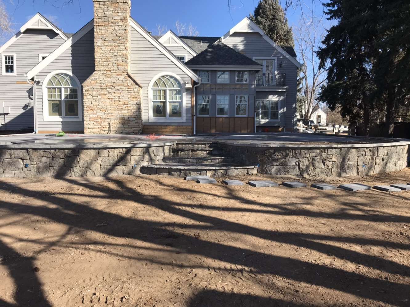 A large house with a stone chimney is sitting on top of a dirt field.