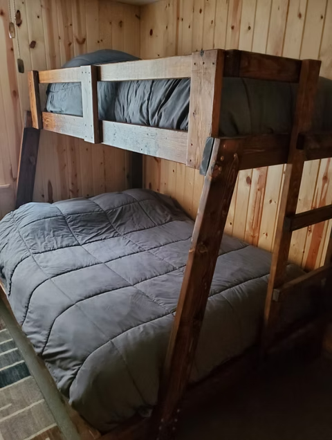 Wooden bunk bed with gray bedding in a wood-paneled room