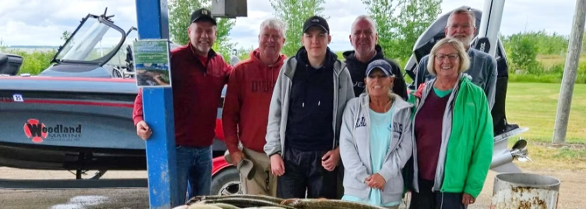Group of six people posing beside a boat at a waterfront dock.