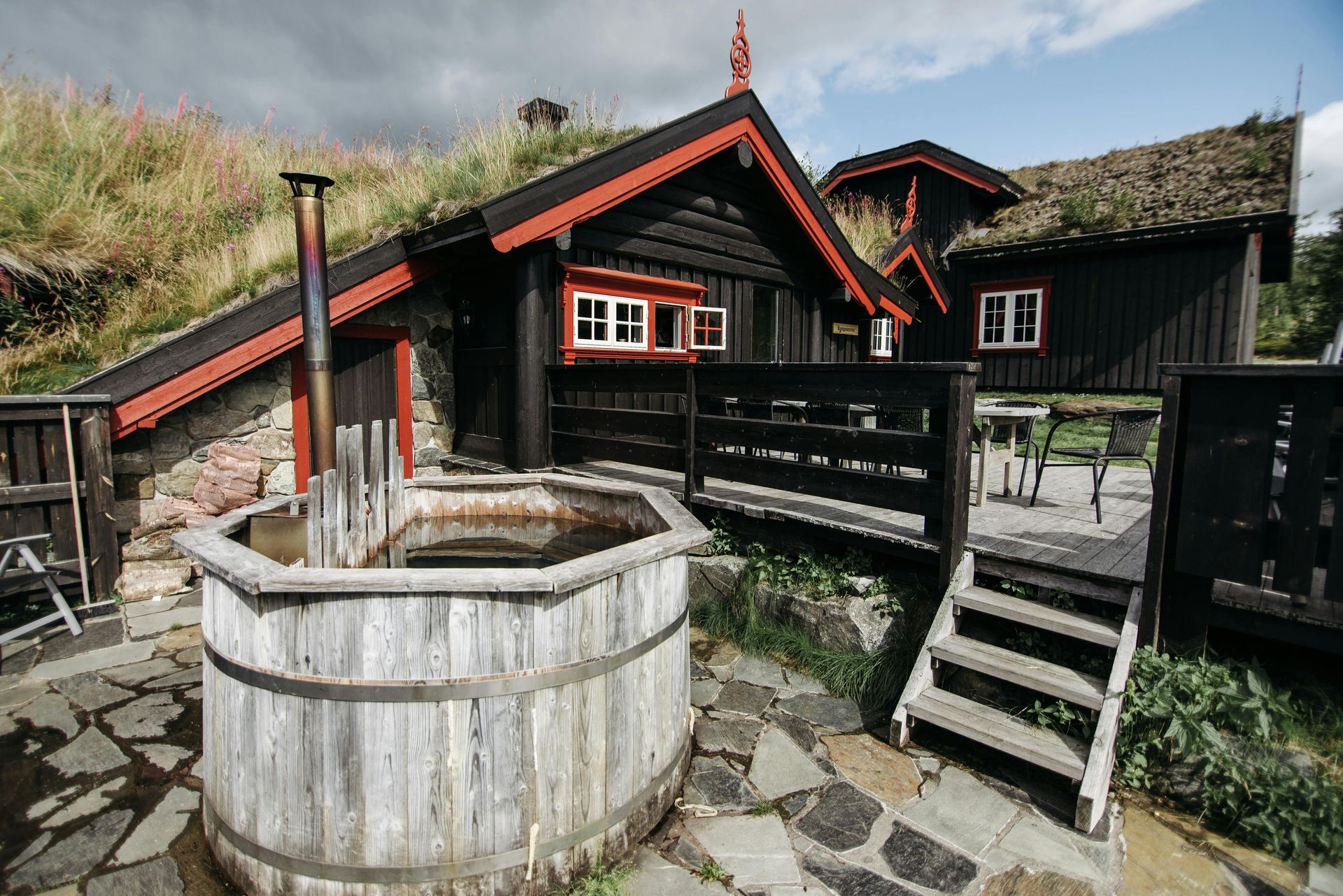 Rustic black-and-red wooden cabins beside a stone path and wooden water tub in a mountain village