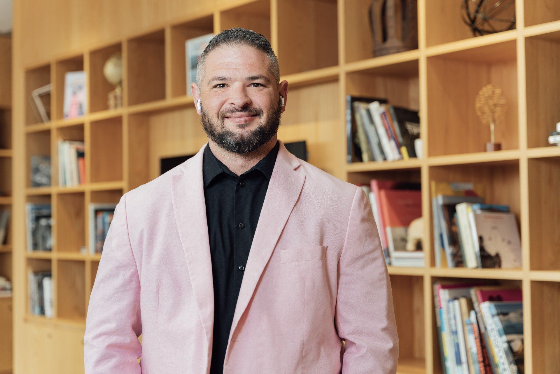 a man in a pink jacket and black shirt is standing in front of a bookshelf .