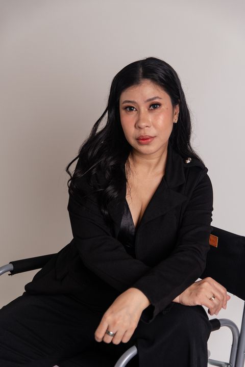 A woman in a black suit is sitting in a chair.