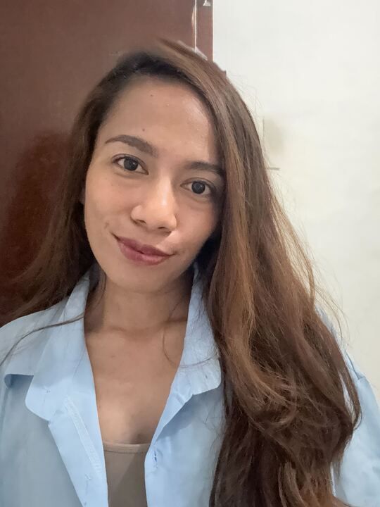 A woman with long brown hair is wearing a blue shirt and smiling.