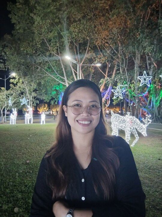 A woman wearing glasses is smiling in front of christmas lights.