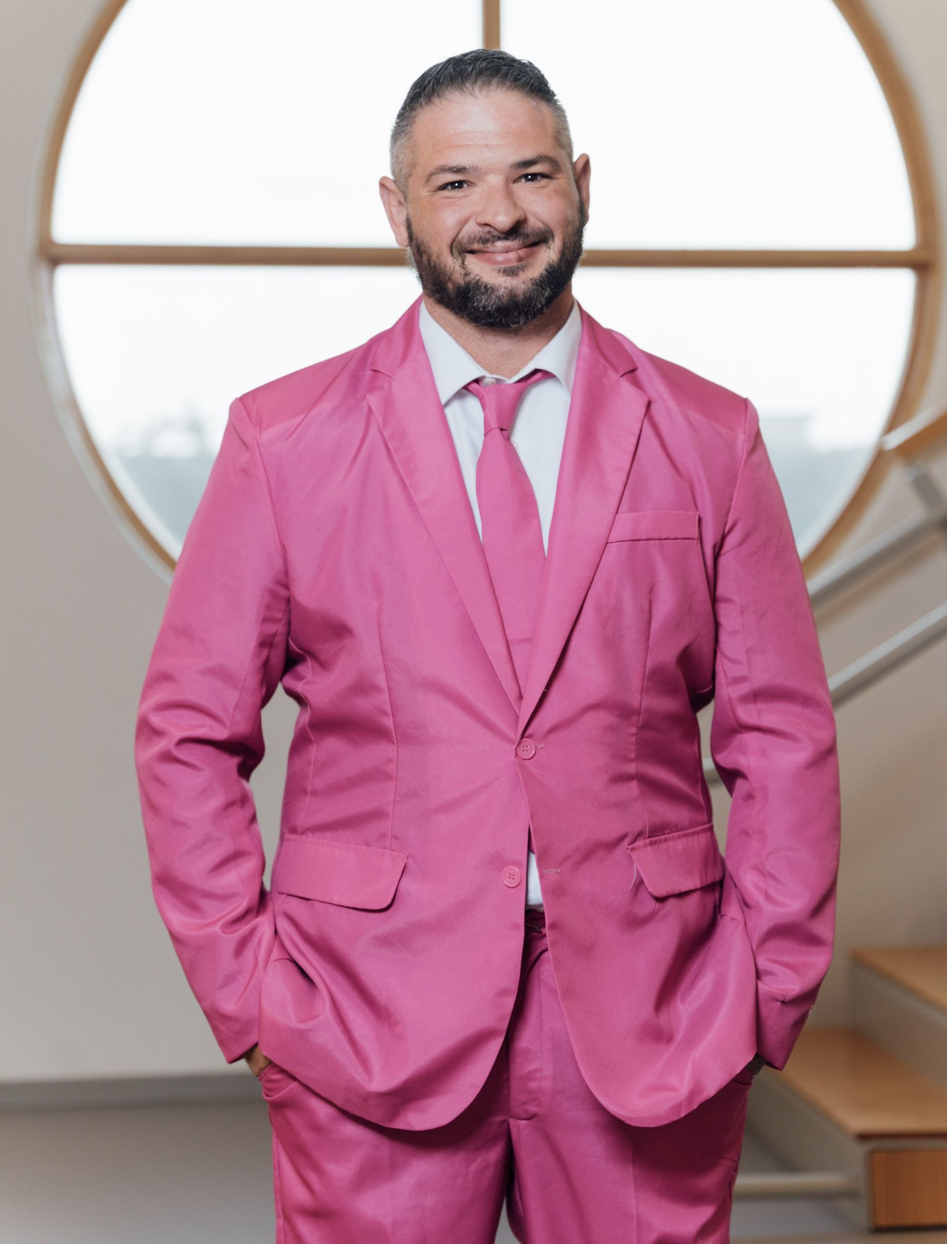 a man in a pink suit and tie is standing in front of a window .