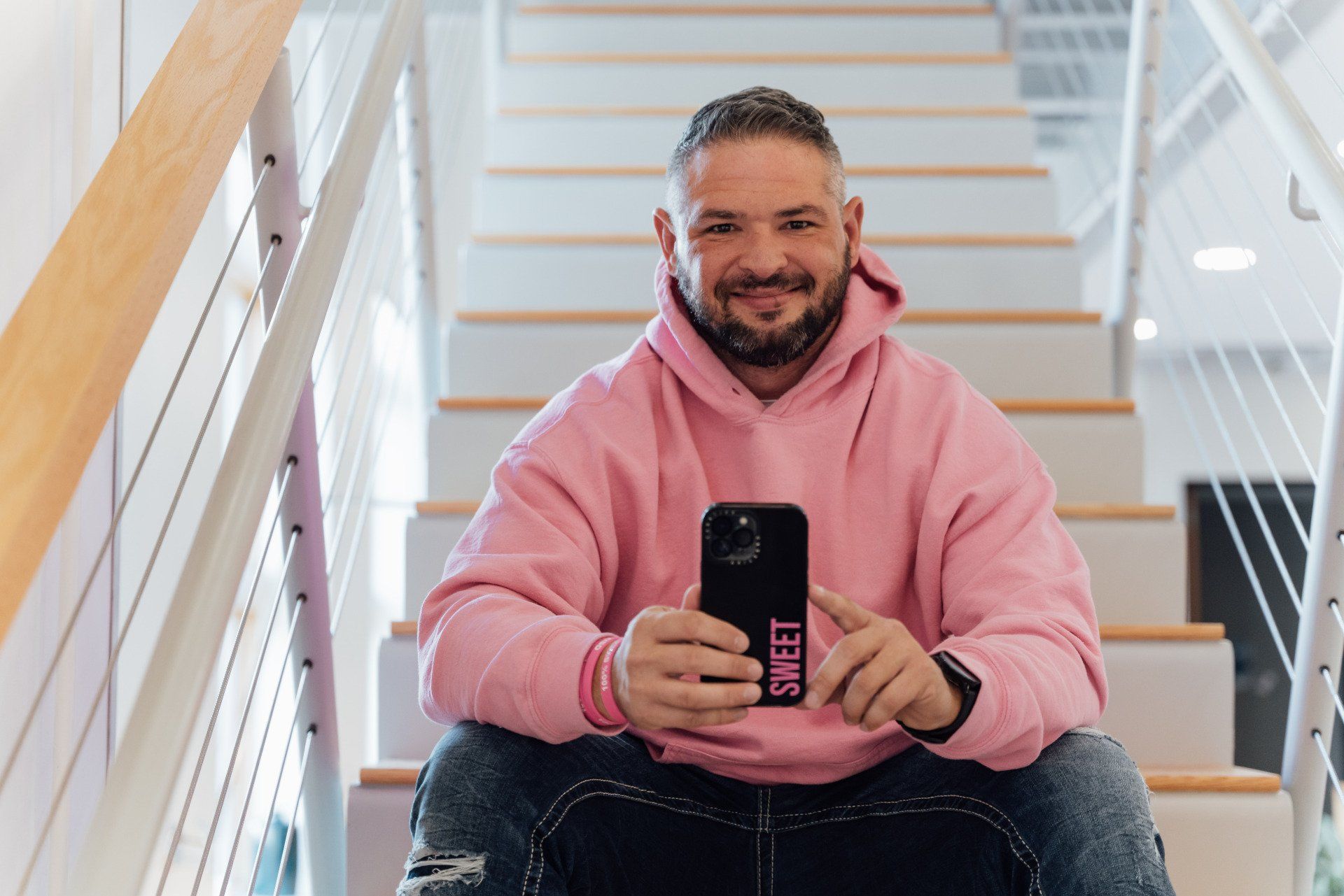 a man in a pink hoodie is sitting on a set of stairs holding a cell phone .