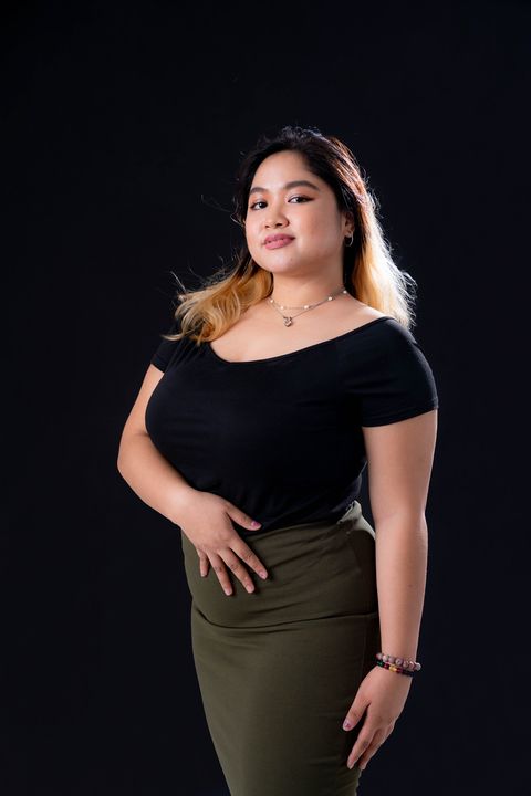 A woman in a black top and green skirt is standing in front of a black background.