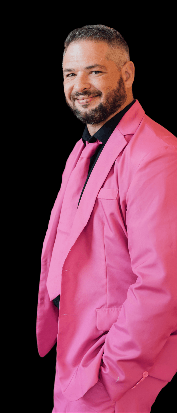 a man in a pink suit and tie is standing with his hands in his pockets .