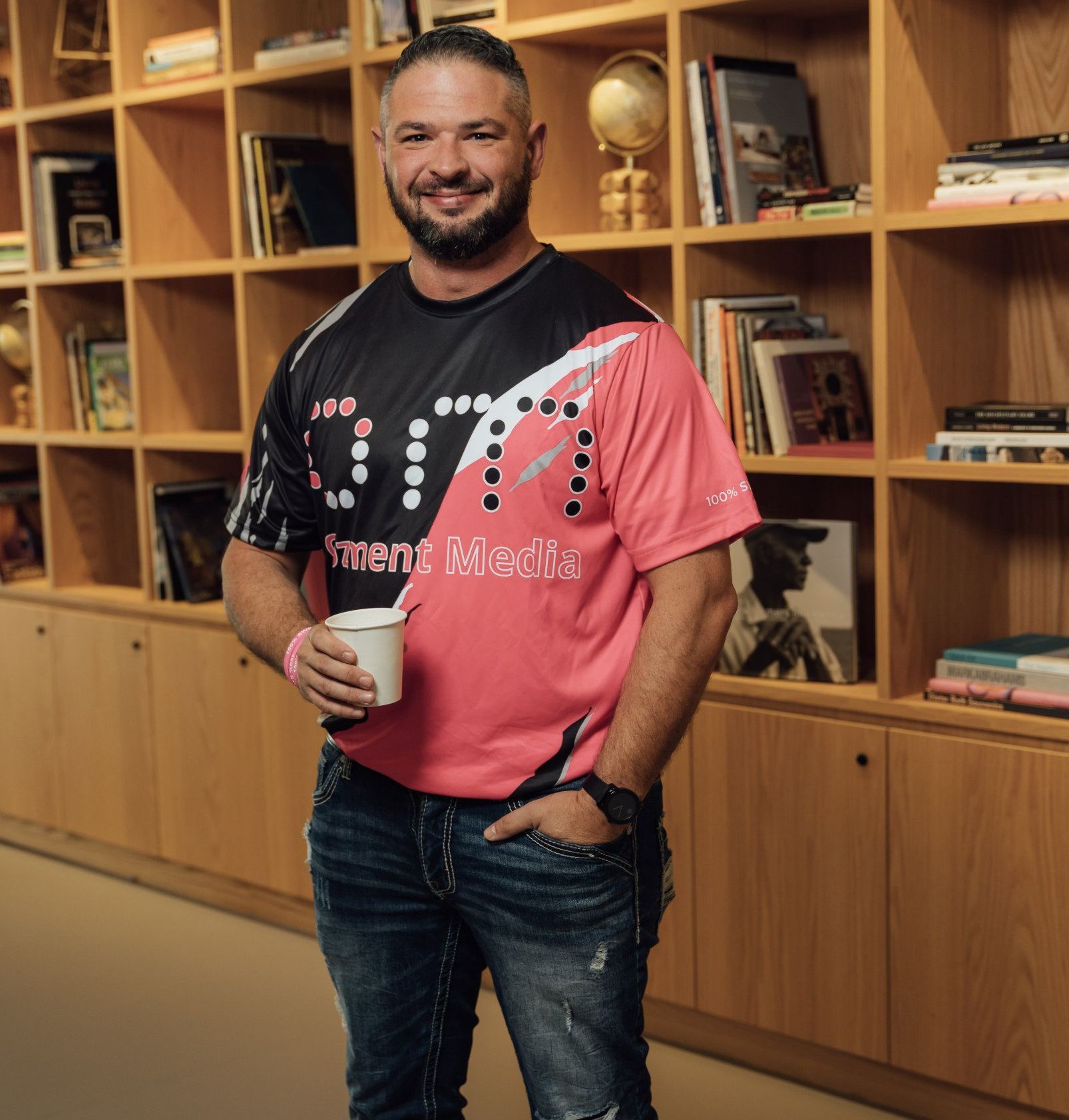 A man wearing a pink shirt that says ' ozment media ' on it