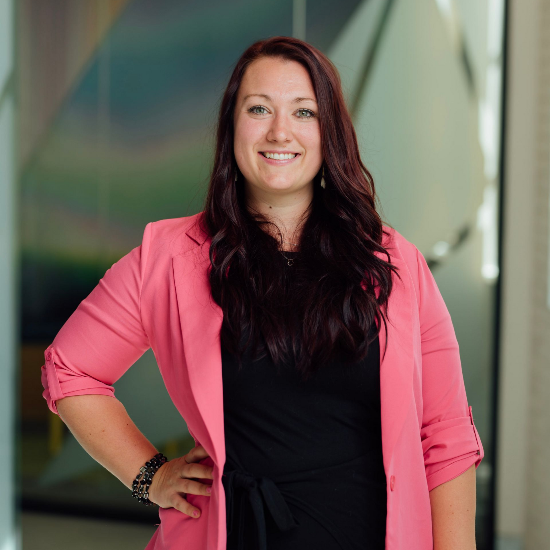 A woman in a pink jacket is standing in a kitchen holding a cup of coffee.