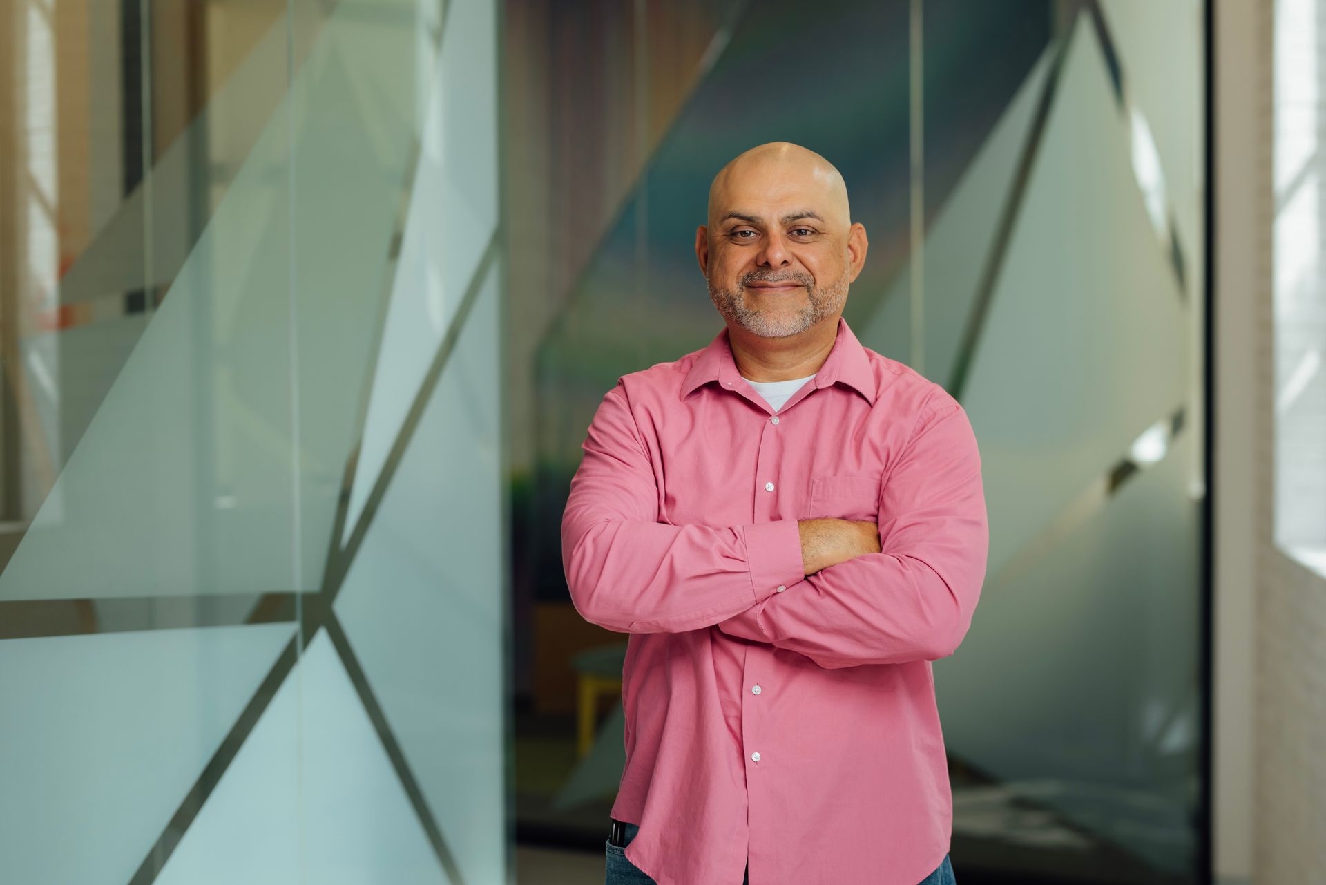 A bald man with a beard is wearing a pink shirt and smiling.