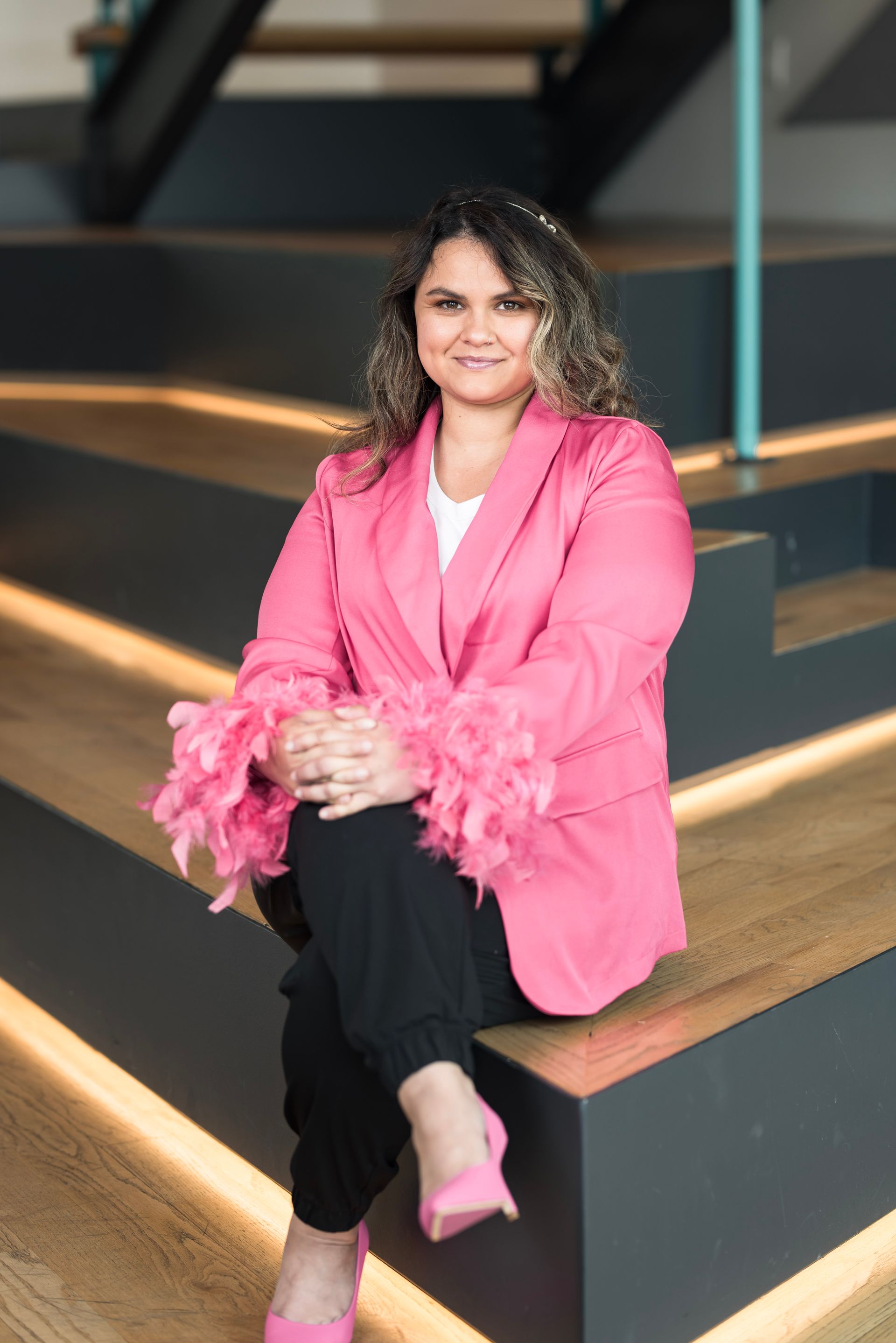 A woman in a pink jacket and pink shoes is sitting on a set of stairs.
