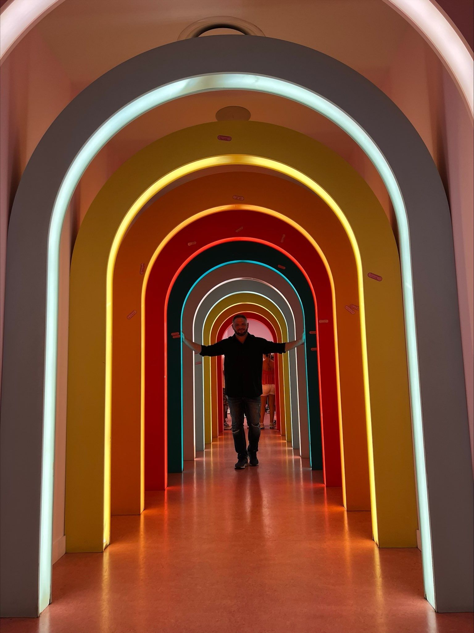 A man is standing in a rainbow colored tunnel with his arms outstretched
