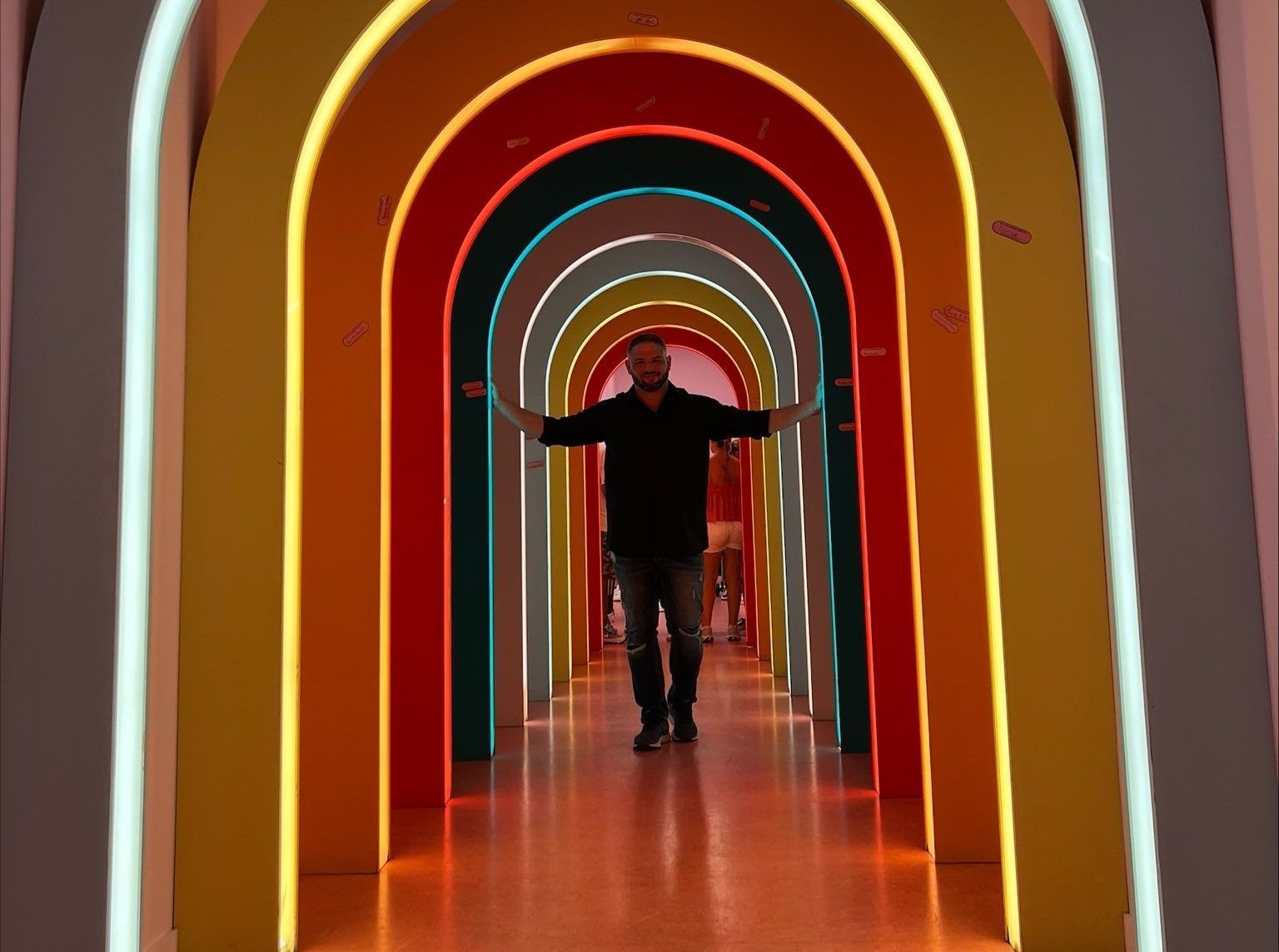 A man is standing in a rainbow colored tunnel with his arms outstretched