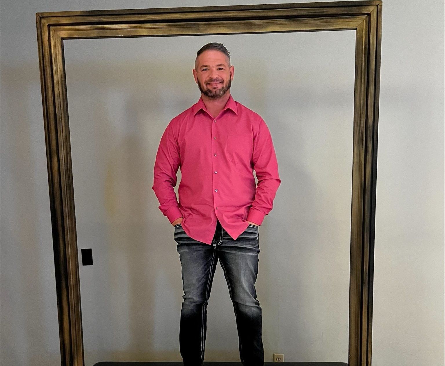 A man in a pink shirt is standing in a picture frame.