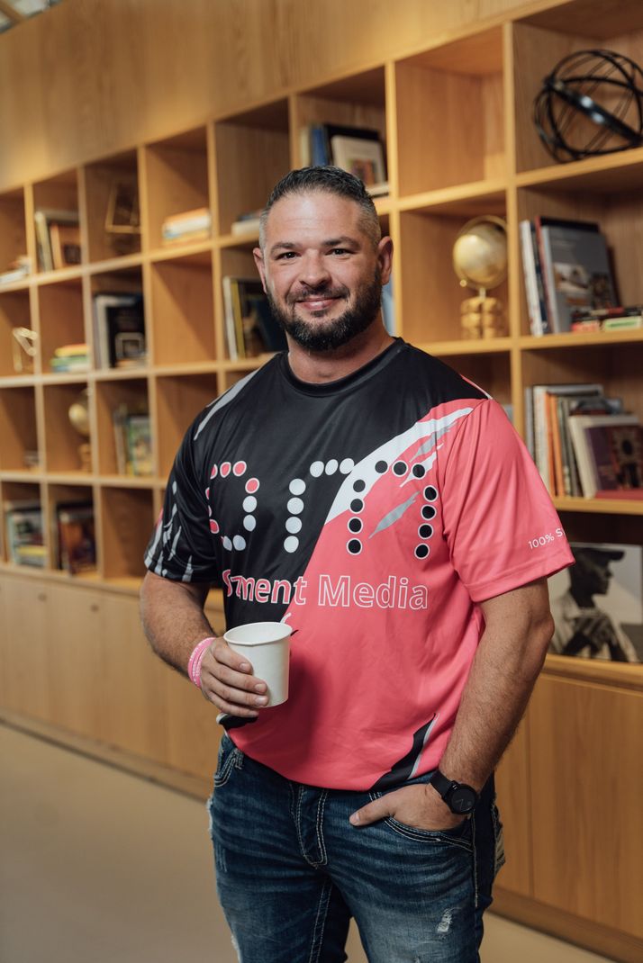 a man in a pink shirt is standing in front of a bookshelf holding a cup of coffee .