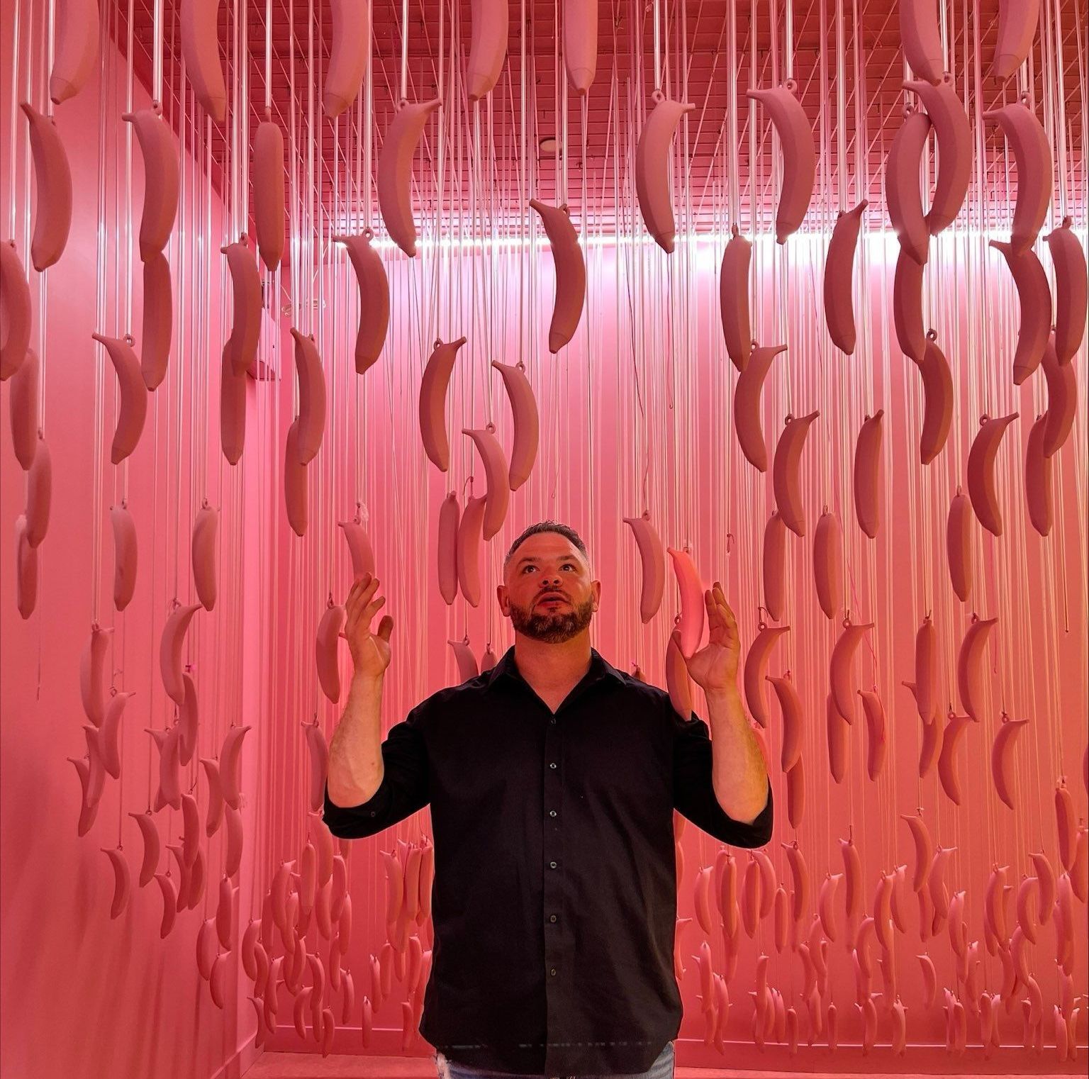 a man is standing in front of a pink wall with bananas hanging from the ceiling .