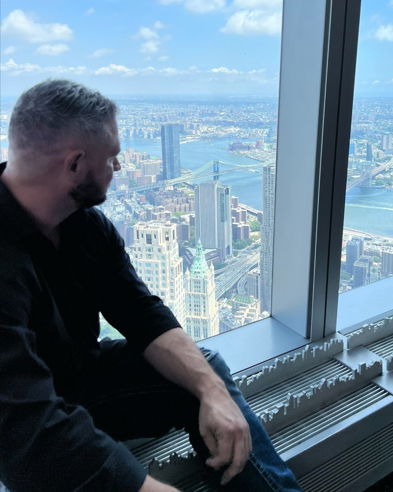 A man is sitting on a window sill looking out over a city