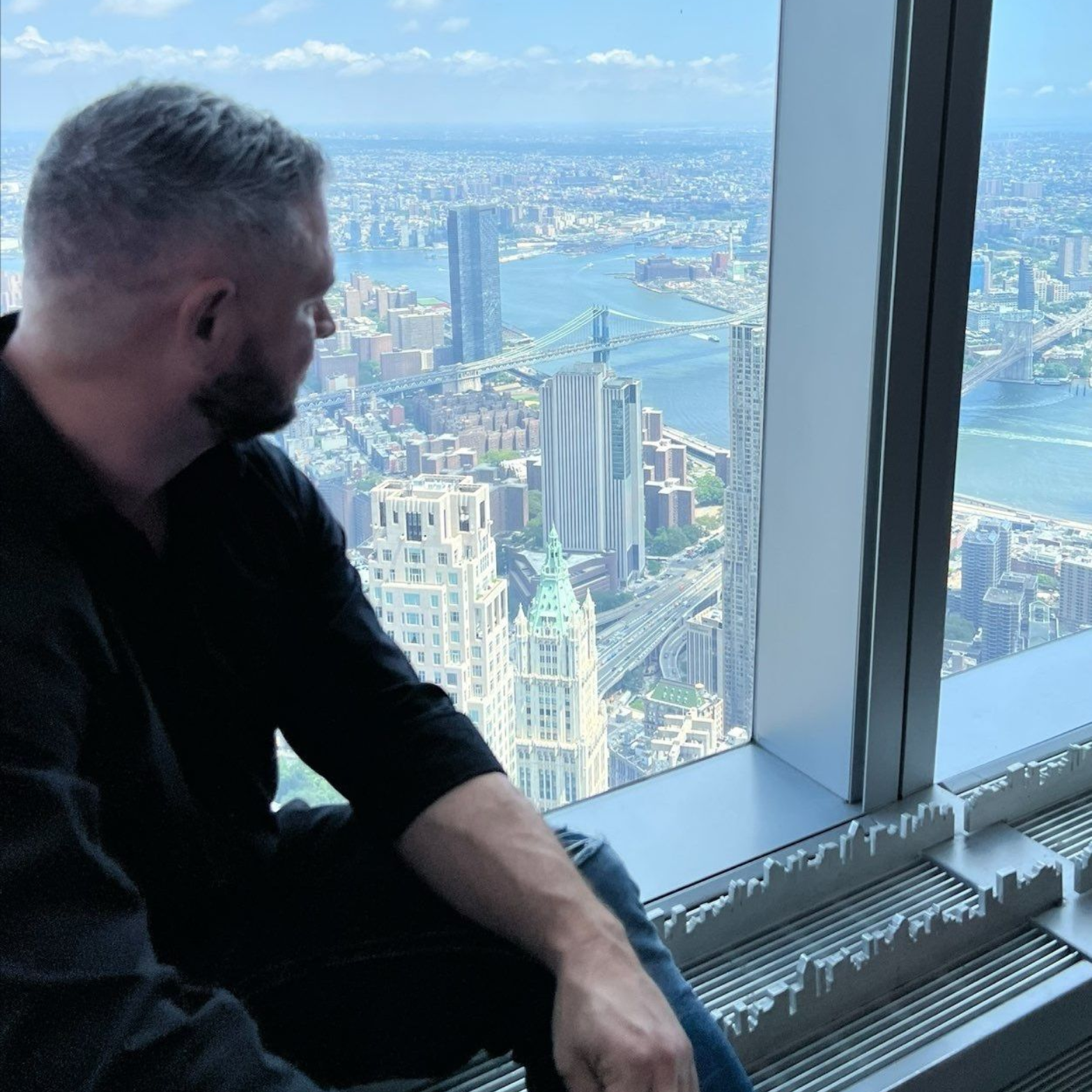 Man looking out a window at a cityscape with blue sky.