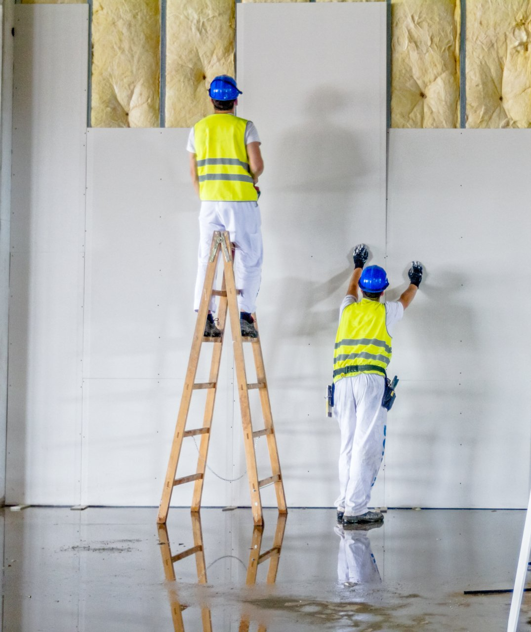 Two construction workers are working on a wall while one is standing on a ladder.