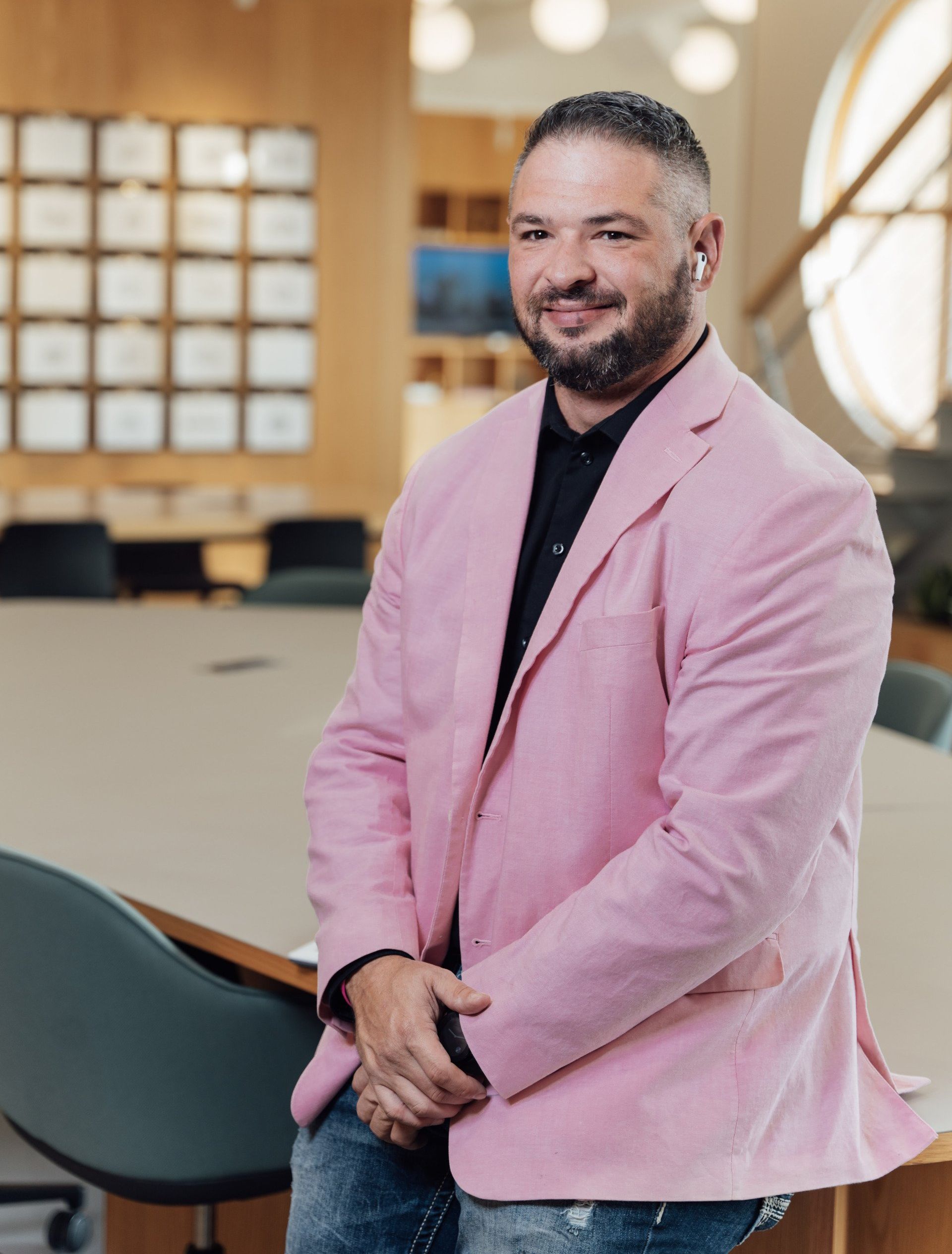 a man with a beard is wearing a pink jacket and sitting on a chair .