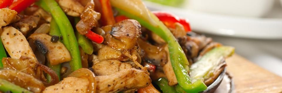 A close-up of a chicken and mushroom stir-fry with sliced green peppers, served on a wooden platter.