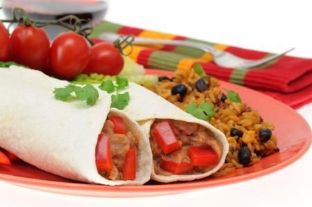 Two bean and red pepper burritos on an orange plate, served with a side of black bean rice and fresh cherry tomatoes.