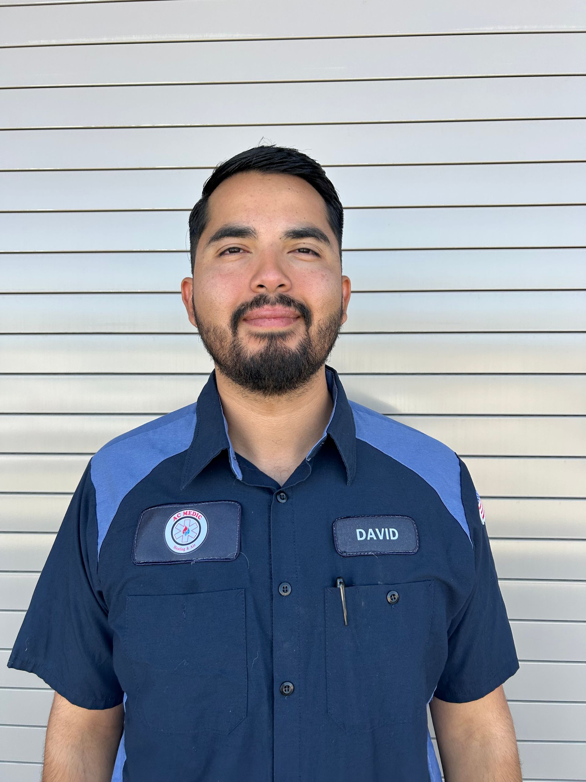 Man in blue work shirt, smiling, in front of a metal rolling door.