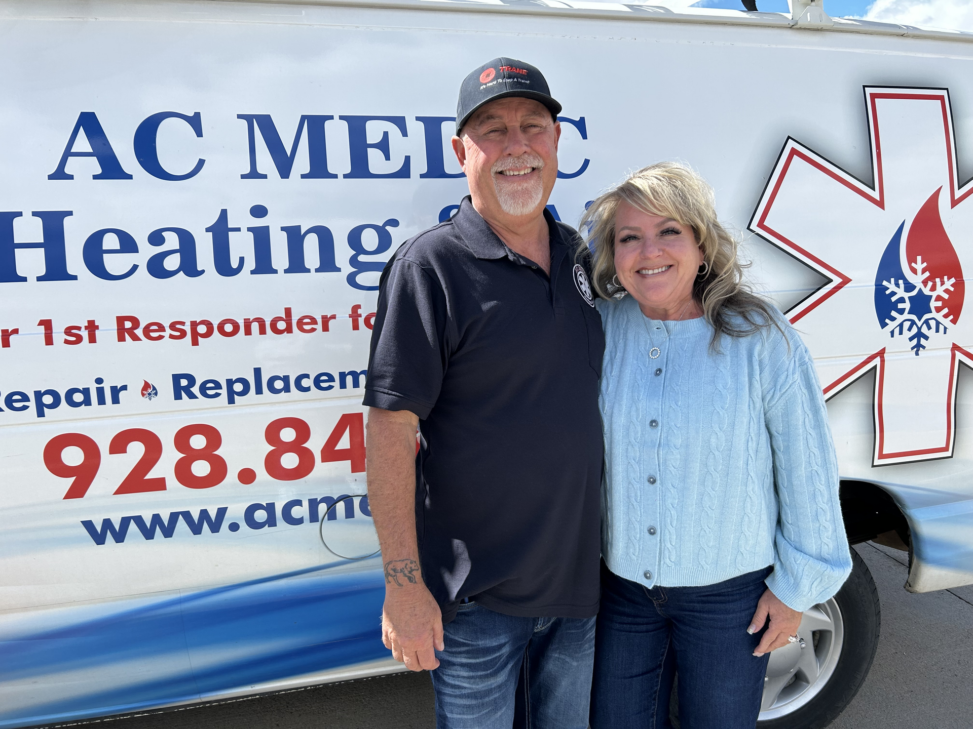 Two people stand in front of an AC Medic truck. A man and a woman smile. Text on the truck advertises heating and AC services.