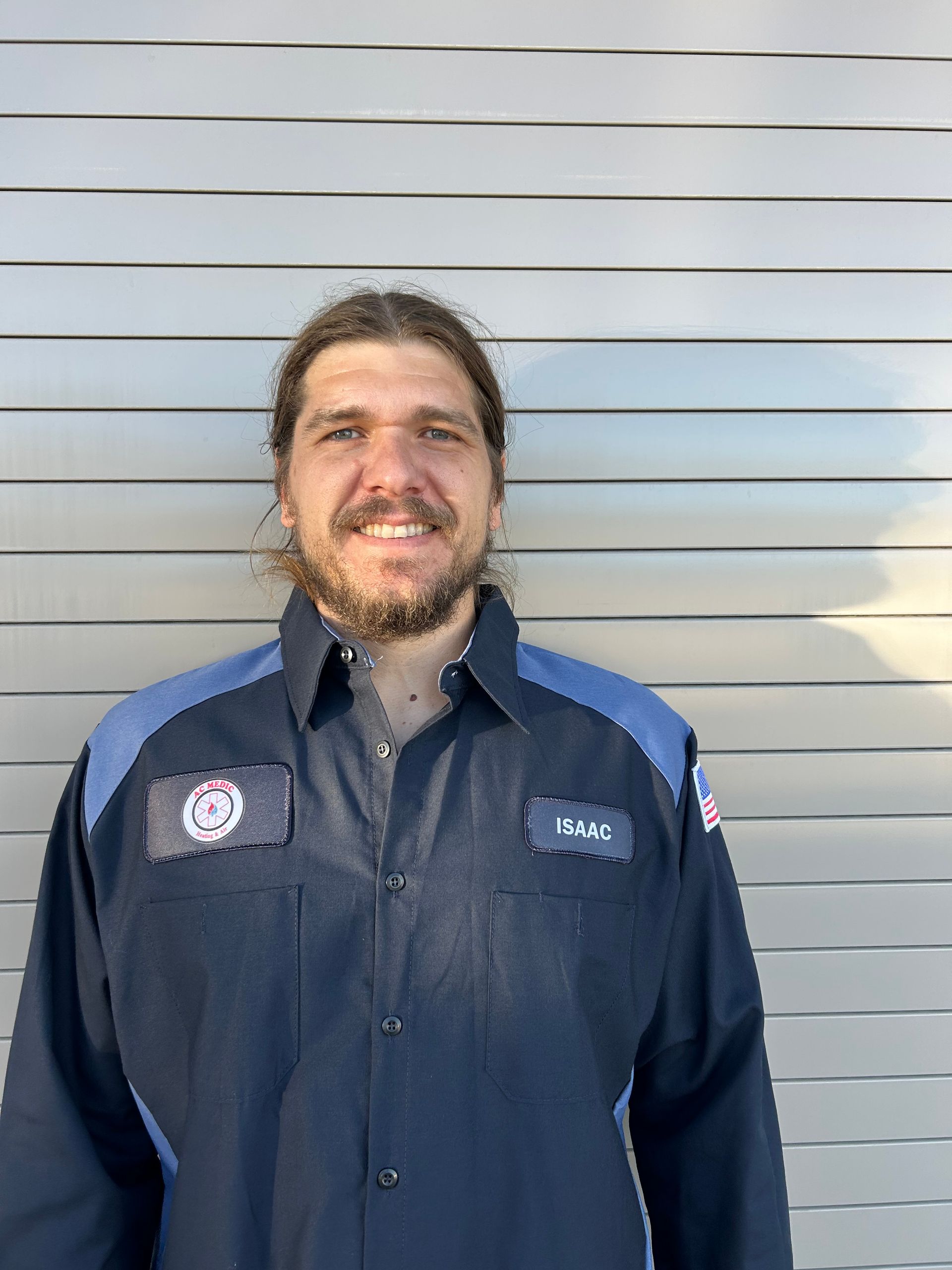 Man in a navy mechanic shirt smiles in front of a gray metal wall.