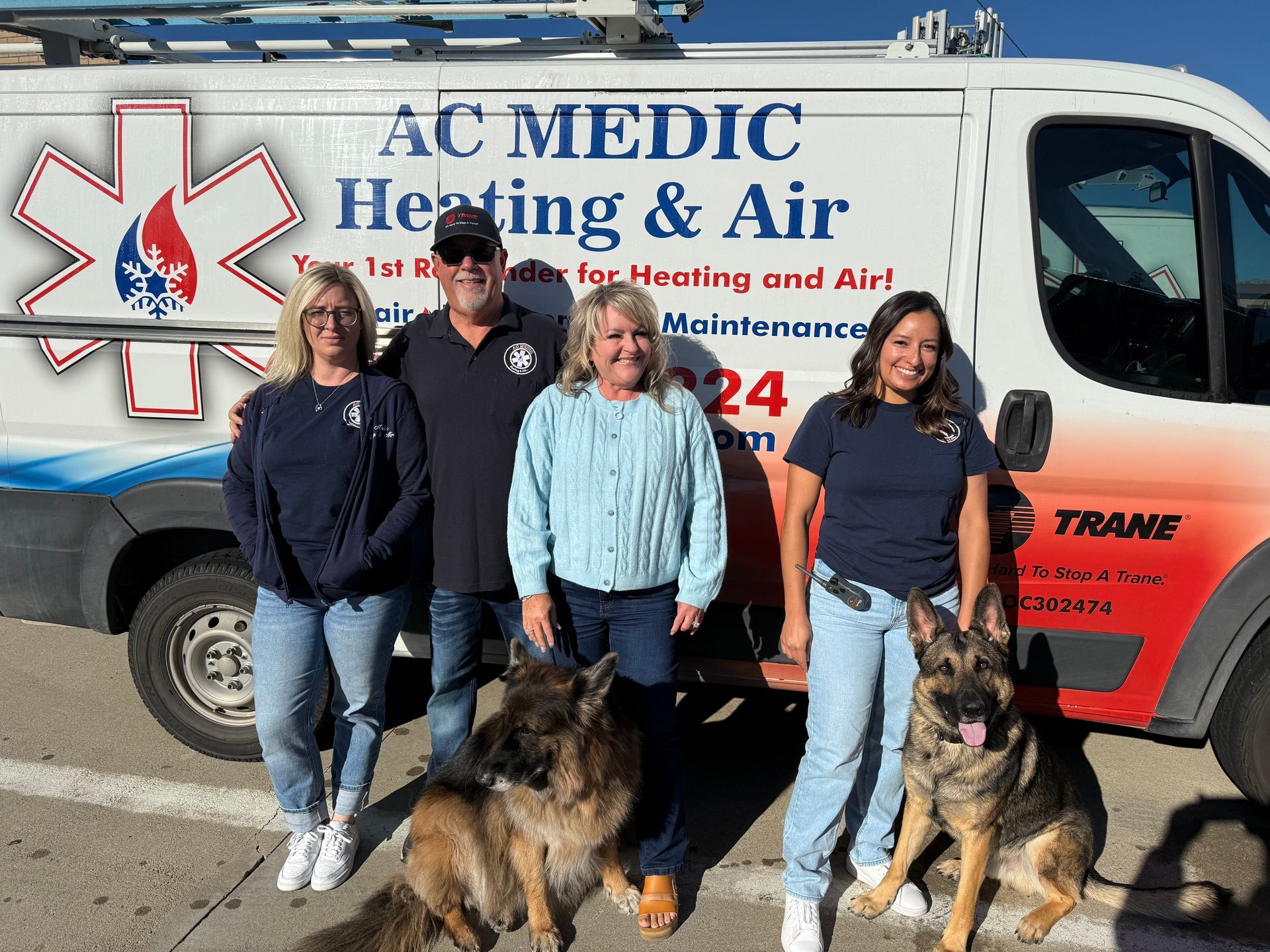 Four people and two German shepherds in front of an AC Medic Heating & Air service van.