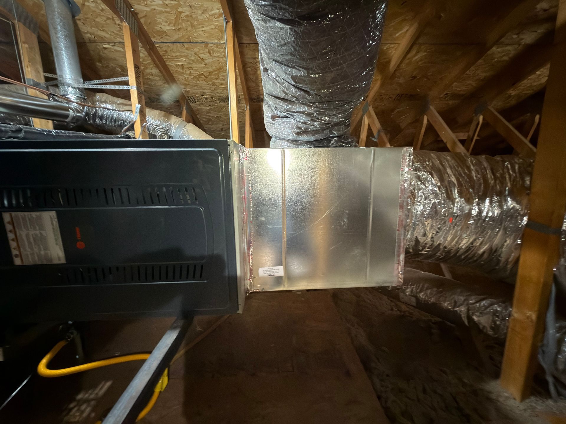 HVAC system in attic: furnace connected to ductwork. Silver metal and insulated flexible ducts.