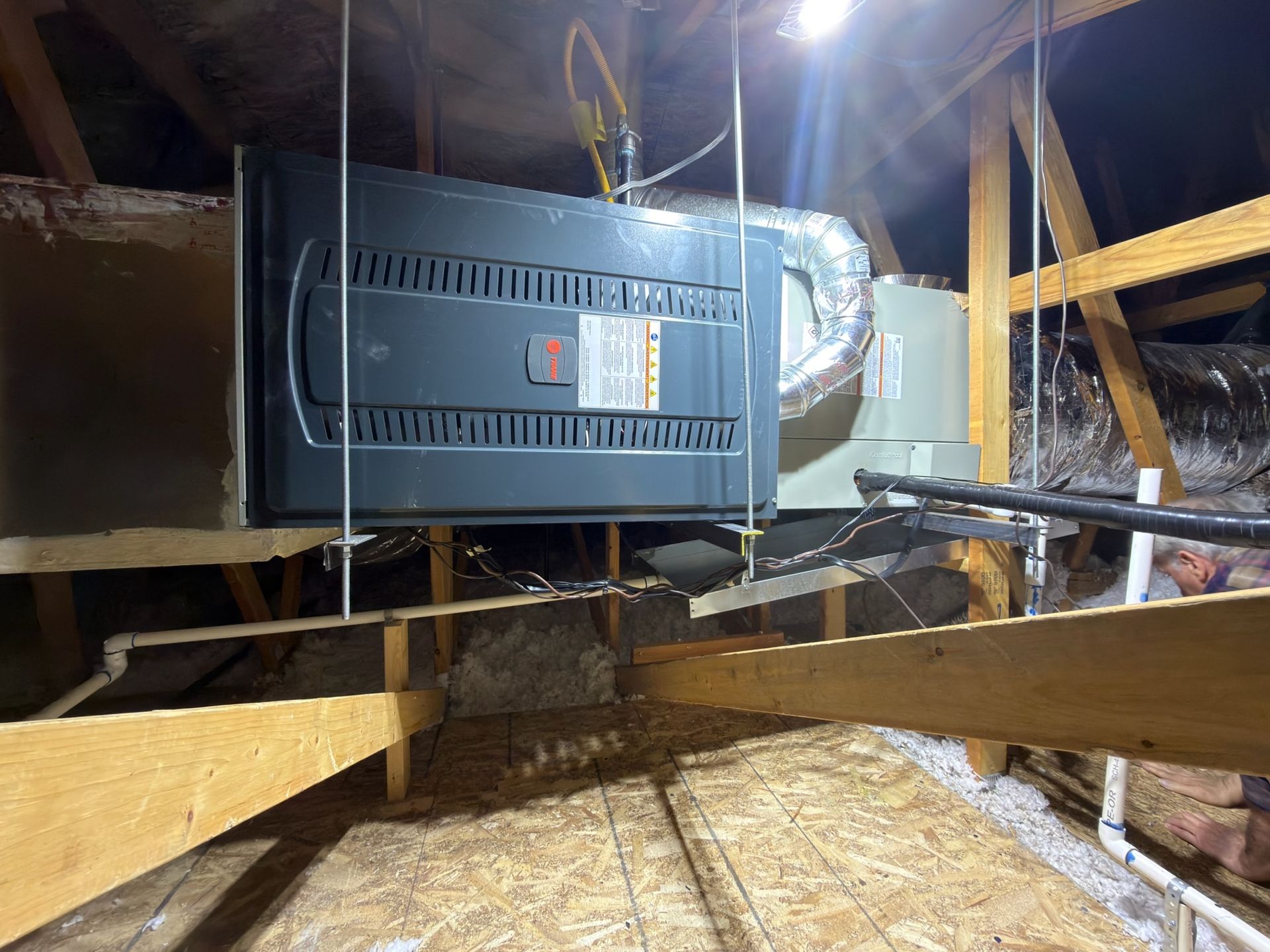 HVAC unit suspended in attic, with ductwork and framing visible.
