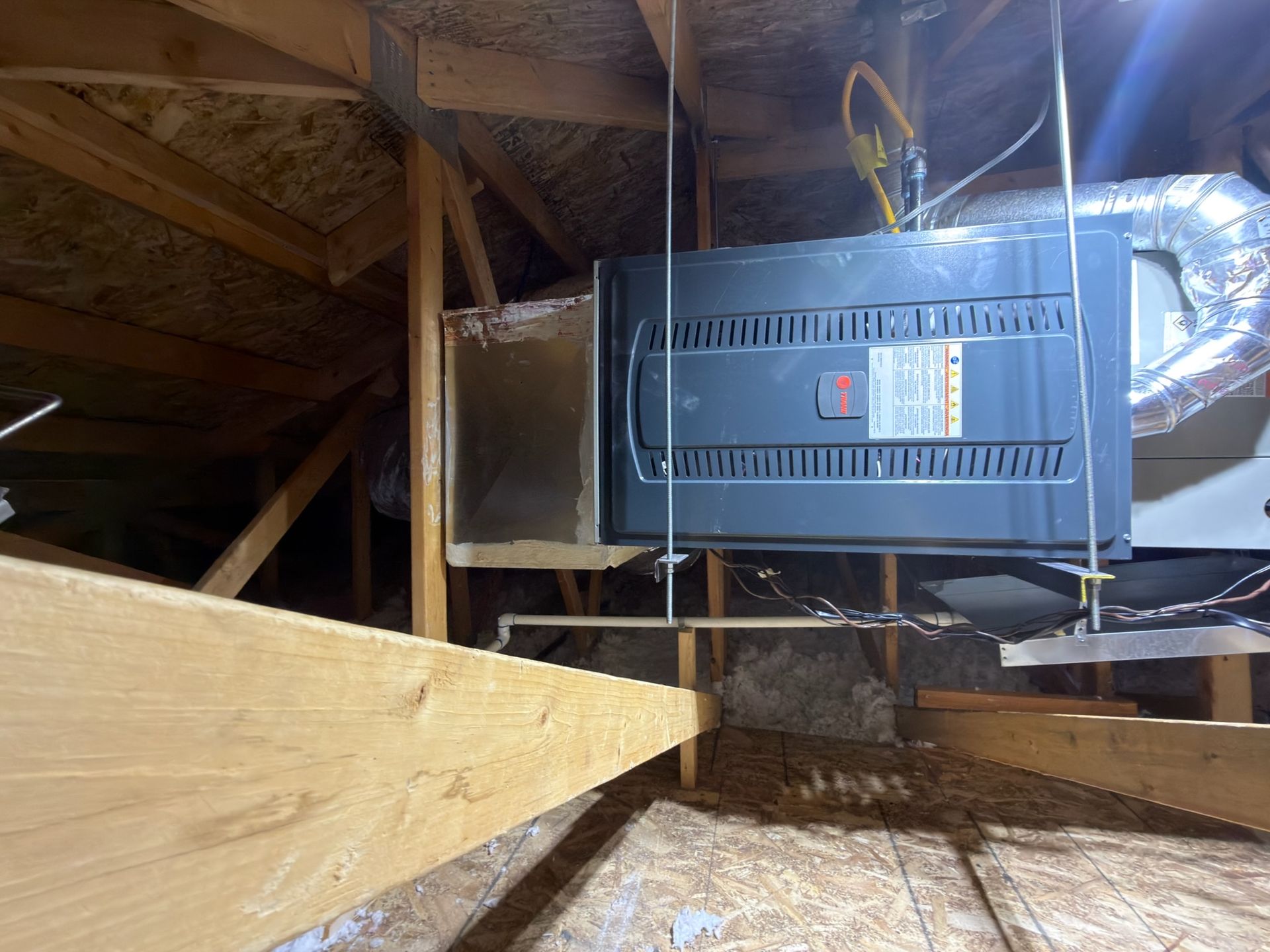 HVAC unit suspended in attic, with ductwork and wooden beams.