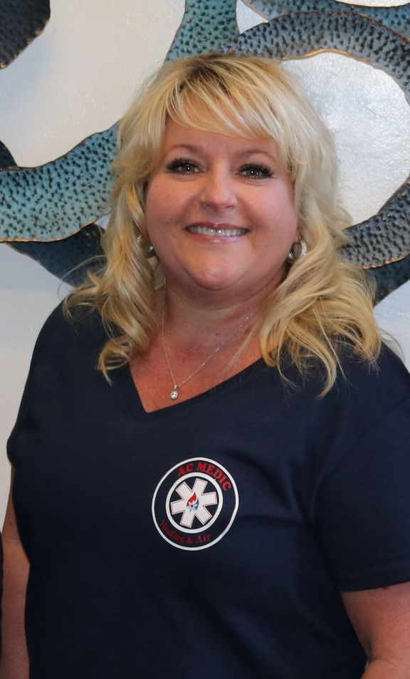 Woman smiling, wearing a navy v-neck shirt with a circular emblem, in front of abstract wall art.