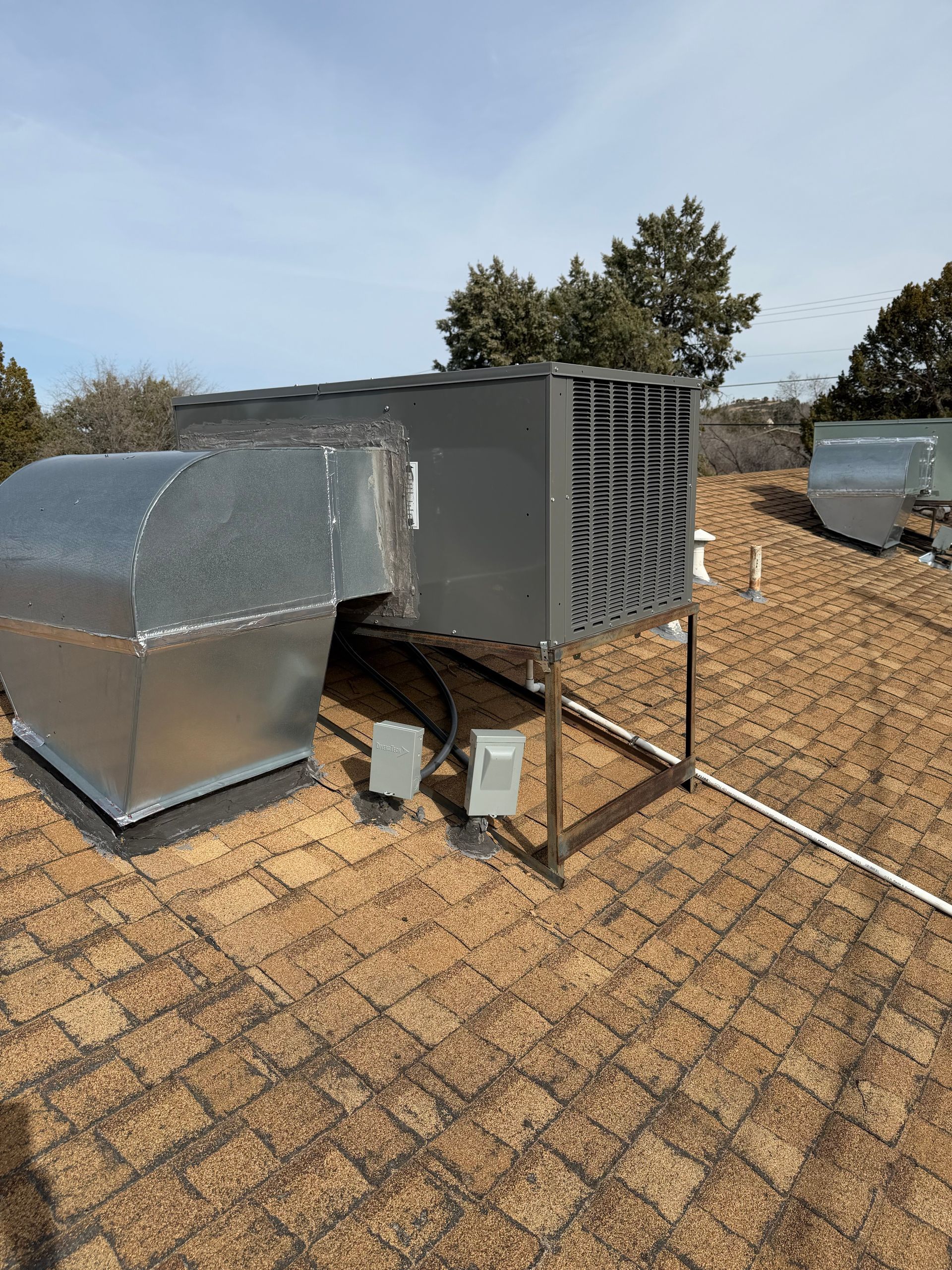 HVAC unit on a rooftop. Gray metal equipment, ducts, and vents against a blue sky.